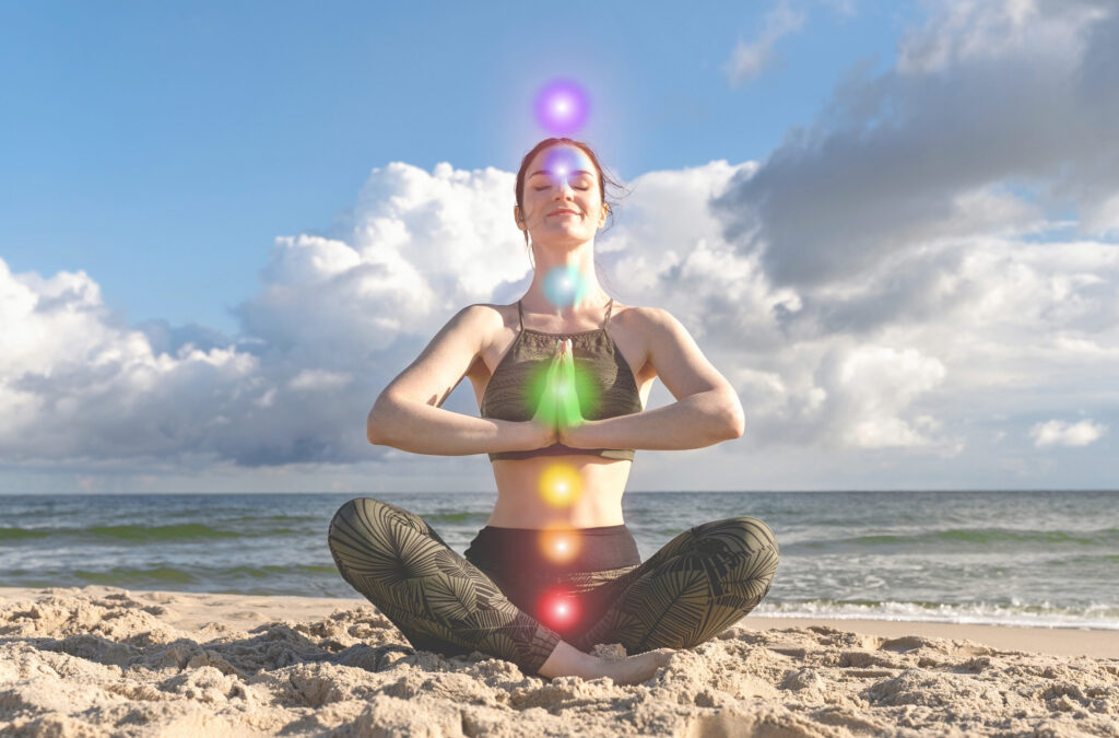 Mujer meditando en la playa con visualización de chakras alineados y activación energética